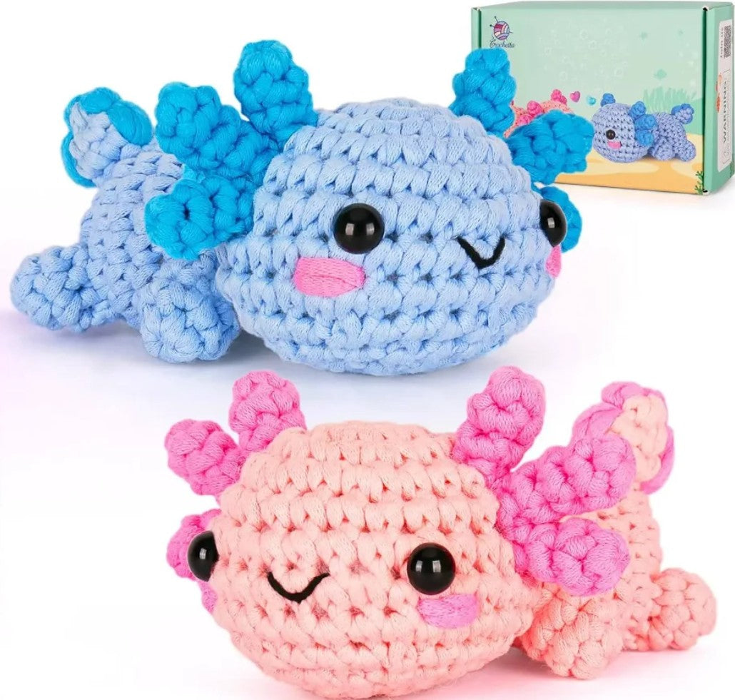Two crocheted axolotl plush toys shown on a white background, one light blue with bright blue spines and one pink with pink spines, plus a small product box in the upper right.