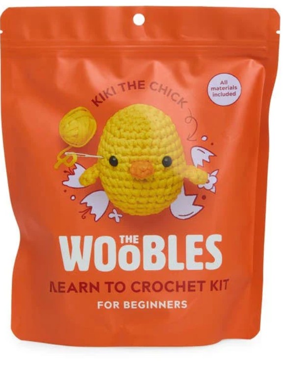 Bright orange stand-up pouch packaging for 'The Woobles Learn to Crochet Kit for Beginners', featuring a yellow crocheted chick illustration and white text on a clean white background.